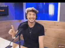 a man wearing headphones and a black shirt is sitting in front of a microphone giving a thumbs up .