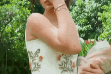 a woman in a white dress with flowers on it is holding a bouquet of flowers .