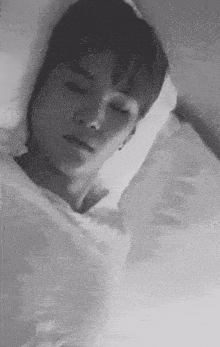 a black and white photo of a young man sleeping on a bed with his eyes closed .