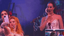 a woman is singing into a microphone while another woman takes a picture of herself .