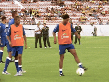 a soccer player wearing an orange nike vest kicks a ball