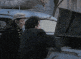 a man in a hat stands next to another man in a black jacket