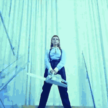 a woman in suspenders is holding a chainsaw in front of a white curtain