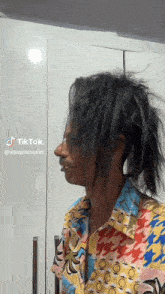a man with dreadlocks and a colorful shirt is standing in front of a white wall .