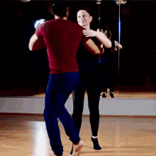 a man in a maroon shirt is dancing with a woman in blue jeans