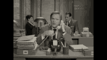 a man sitting at a desk talking on a telephone with a box labeled in