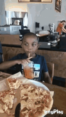 a young boy is drinking through a straw while eating pizza at a restaurant