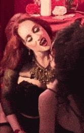 a woman with red hair is kissing another woman with a white candle in the background