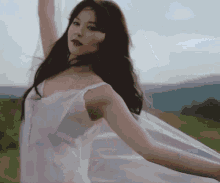 a woman in a white dress is dancing in a field with her arms outstretched