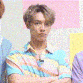 a young man in a colorful shirt is standing with his arms crossed in a room .
