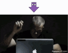 a man is sitting in front of an apple laptop with a purple arrow pointing down