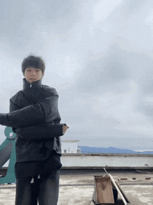 a man in a black jacket is standing on a rooftop with his arms crossed