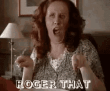 a woman is sitting on a couch with her mouth open and the words `` roger that '' written on her face .