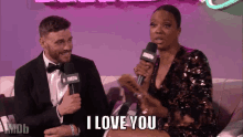 a man and a woman are sitting on a couch and the woman is holding a microphone and saying i love you