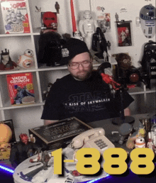 a man wearing a star wars shirt sits at a table surrounded by star wars memorabilia