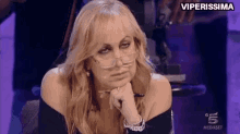 a woman wearing glasses is sitting with her hand on her chin and the words viperissima are above her .