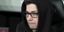 a man wearing glasses and a black hoodie has the letter v on his back