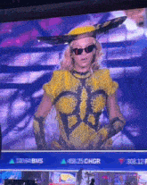 a woman in a yellow outfit is standing in front of a screen that says " bms " on it