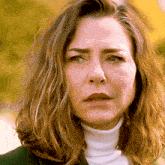 a woman wearing a white turtleneck looks at the camera with a serious look on her face