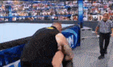 a man is kneeling down in a wrestling ring while a referee stands nearby .