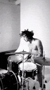 a man without a shirt plays drums in a black and white photo