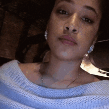 a woman wearing a blue sweater and silver earrings is taking a selfie