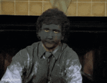 a man with gray paint on his face is sitting in front of a fireplace ..