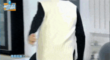 a person wearing a white vest and black sleeves is standing in front of a refrigerator .