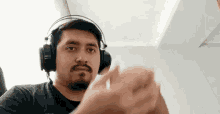 a man with a beard wearing headphones is clapping his hands in a room .