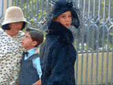 a woman wearing a fur coat and a hat stands next to a boy