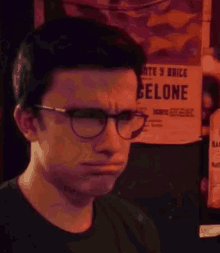 a man wearing glasses and a black shirt is making a funny face in front of a poster .