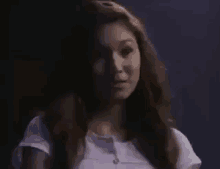 a woman in a white shirt is standing in a dark room looking at the camera .