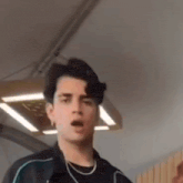 a young man in a black jacket is making a funny face in a room .