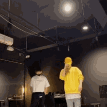 a man in a yellow sweatshirt is singing into a microphone while another man looks on .