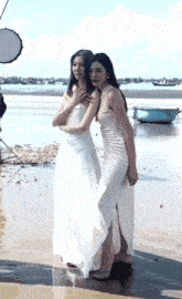 two women in white dresses are posing for a picture on a beach