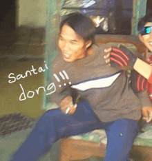 a man with santai dong written on his shirt is sitting on a couch