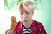 a young man in a red shirt is eating a fried chicken leg .