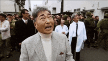 a man in a suit and white coat is standing in a crowd of people .