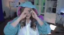 a woman wearing a blue and pink hoodie is covering her eyes with her hand .