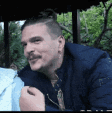 a man with a bun on his head and a blue jacket is smiling