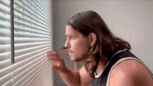 a man with long hair and a beard is looking out a window .
