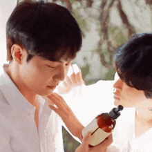a man in a white shirt is touching another man 's face and holding a bottle