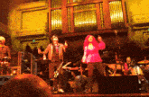 a group of people standing on a stage with a large organ in the background