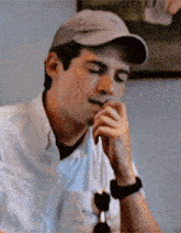 a man wearing a hat and a watch is sitting at a table with his hands on his chin .