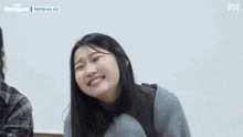 a girl in a blue sweater is smiling in front of a white wall