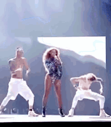 a woman is singing into a microphone while two men are dancing behind her .