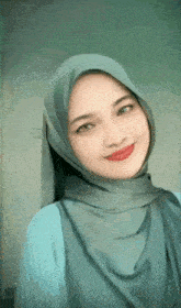 a woman wearing a hijab and a blue shirt is smiling