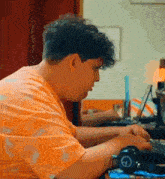 a man in an orange shirt is typing on a laptop .