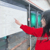a woman in a red sweater is pointing at a map with korean writing on it