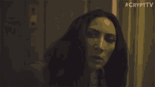 a woman with long dark hair is standing in a dark room looking out a window .